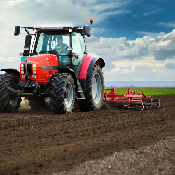 Close-up of griculture red tractor cultivating field over blue sky