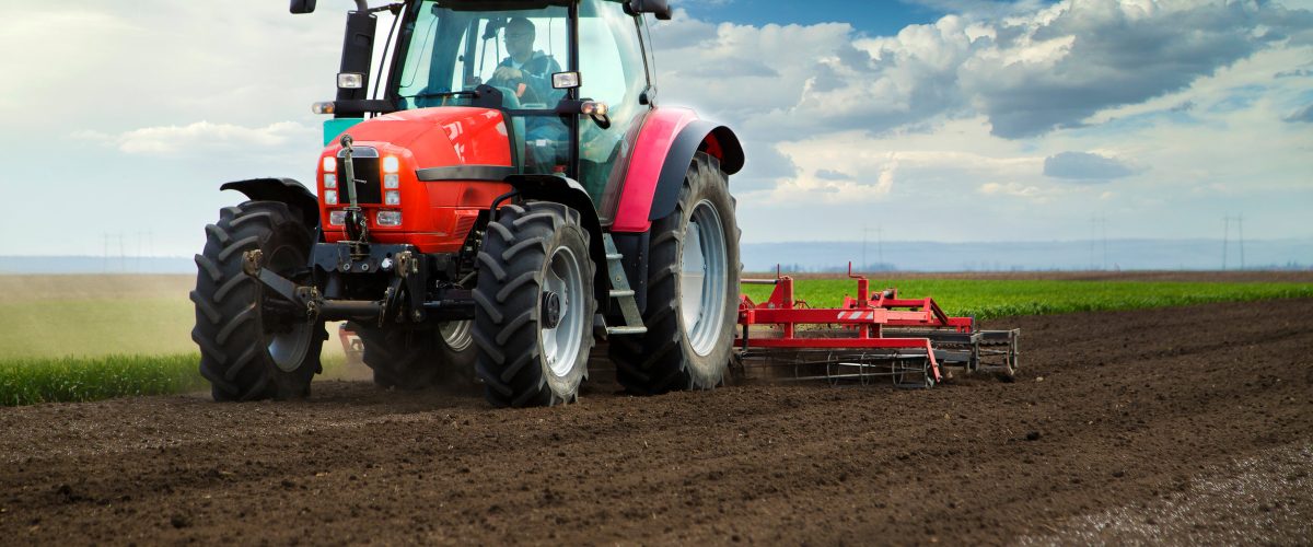Close-up of griculture red tractor cultivating field over blue sky